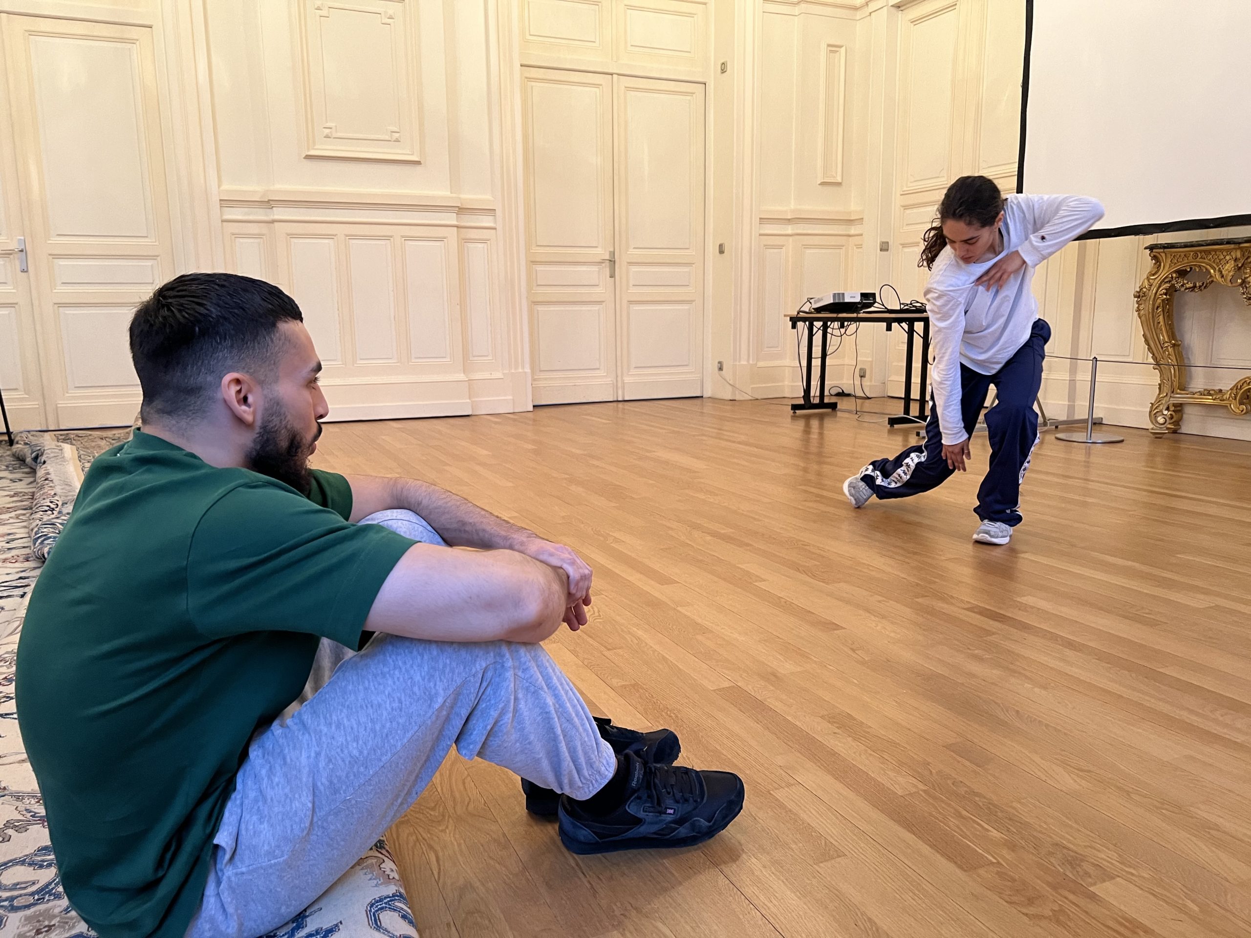 Marouane de la Cie S'Poart, assis au premier plan, qui regarde sa collègue Audrey, en démonstration de breakdance. 