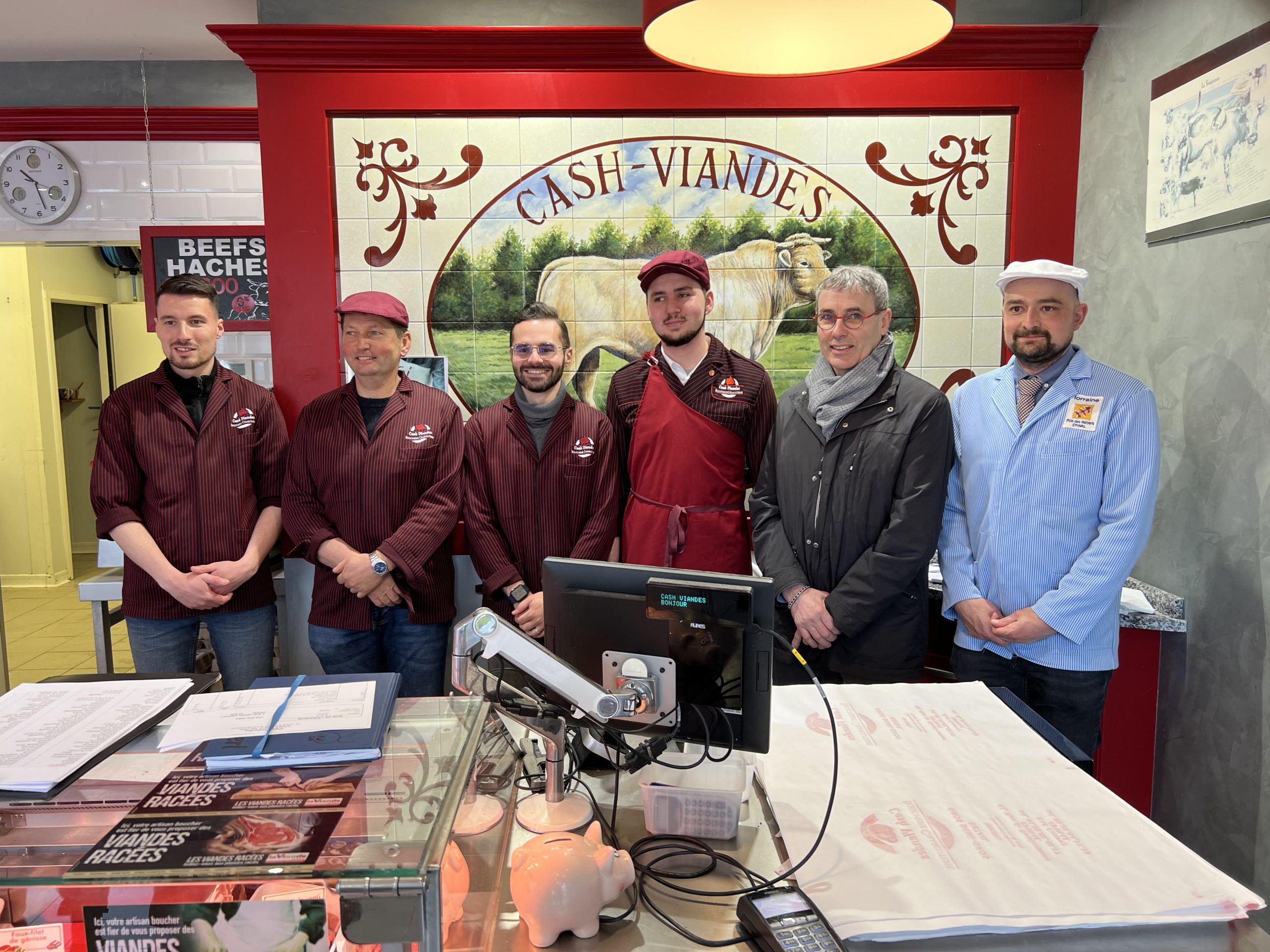 Hugo Blaudez pose dans sa boucherie Cash Viandes, avec à sa gauche le président de la CMA Vosges Christophe Richard et Teddy Géhin son formateur au CFA Pôle des Métiers. A sa droite, Nicolas Bombarde (ex-MAF Boucherie), son papa Dominique et un collègue de la boucherie.