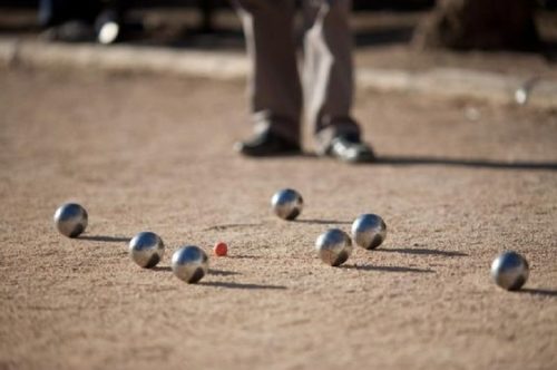 Photo de boules de pétanques sur un terrain, avec un joueur en fond.